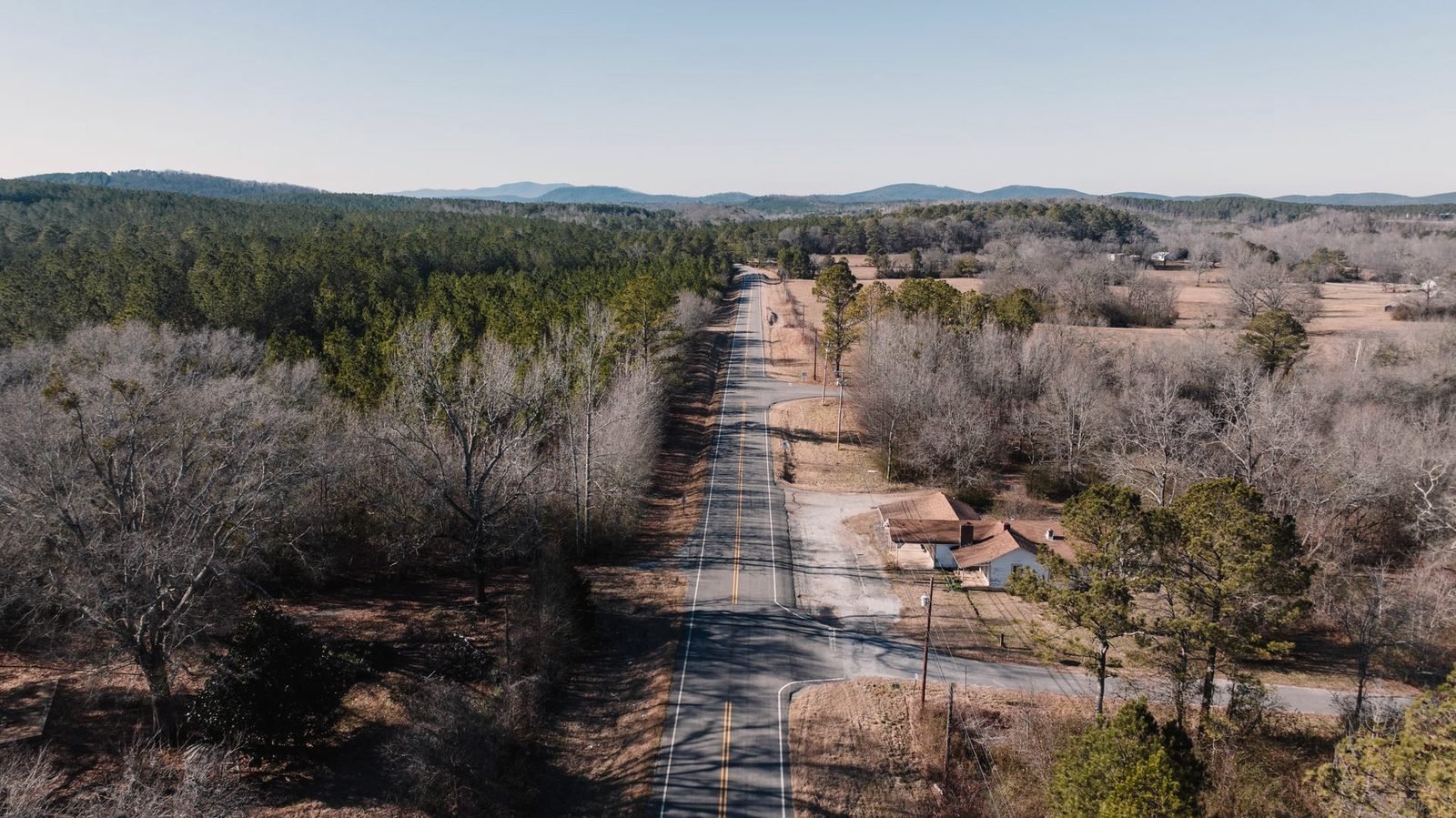 Aerial view of a straight country road through bare winter woods and fields in Alabama