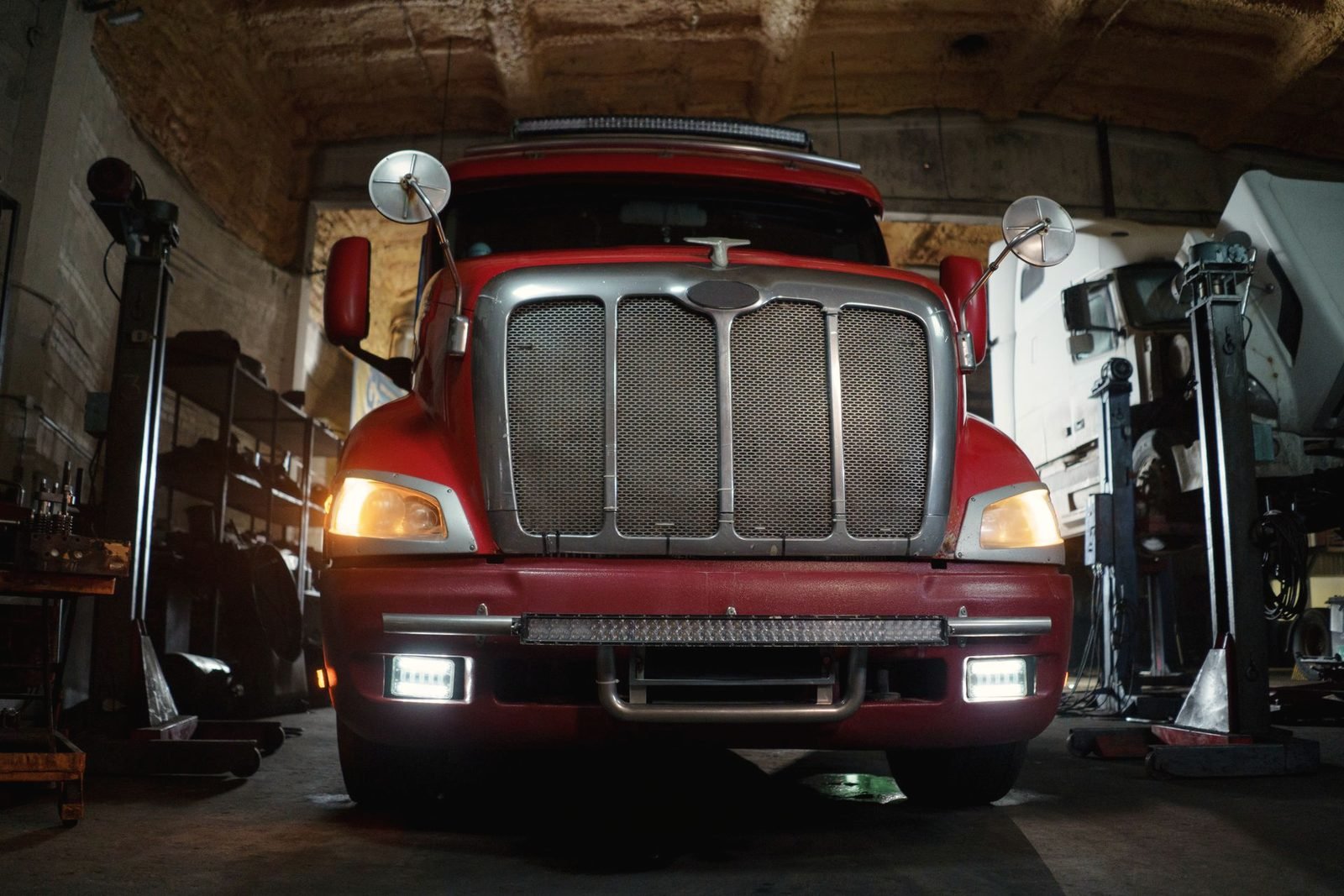 A red tractor parked head-on in a shop bay with its lights on